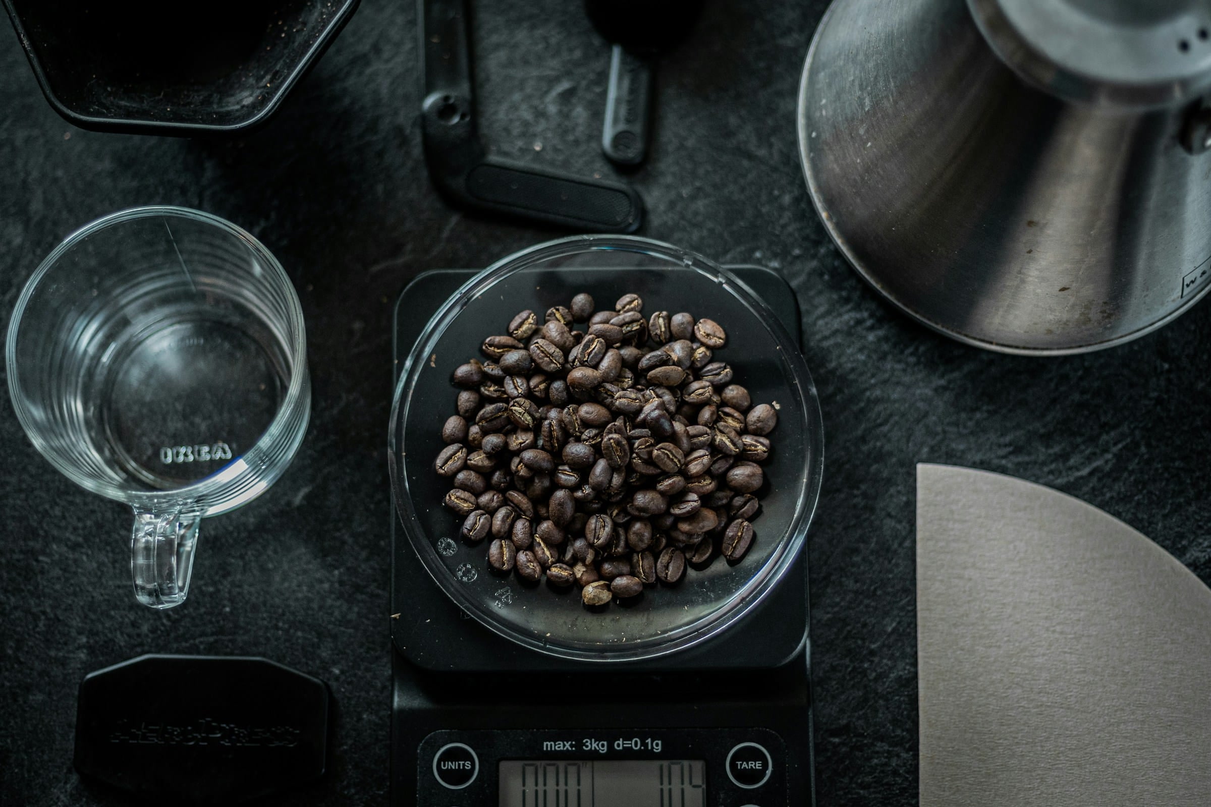 Coffee beans on a digital scale with a cup and grinder in the background