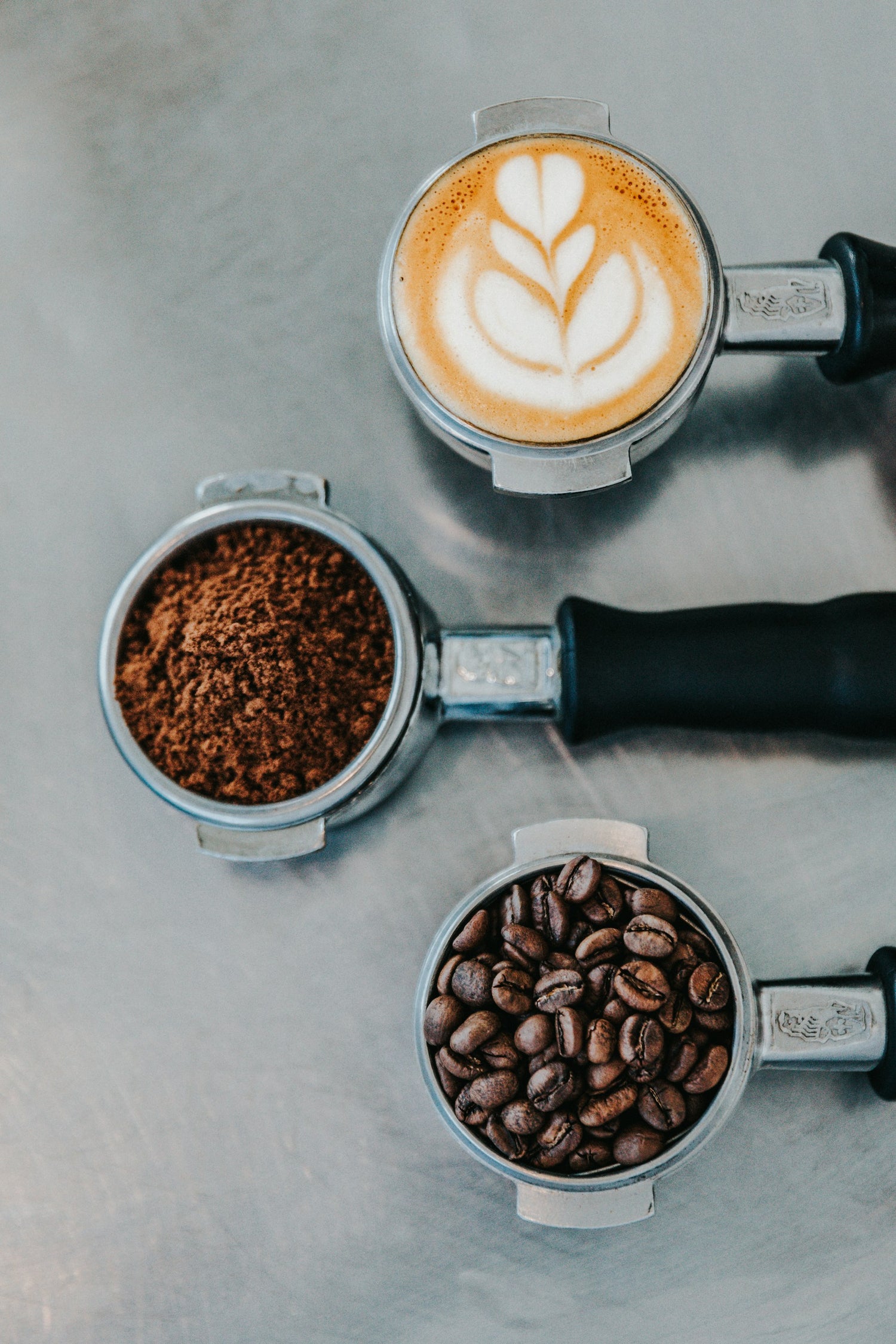 Coffee-making process with a portafilter, ground coffee, and coffee beans on a gray surface.