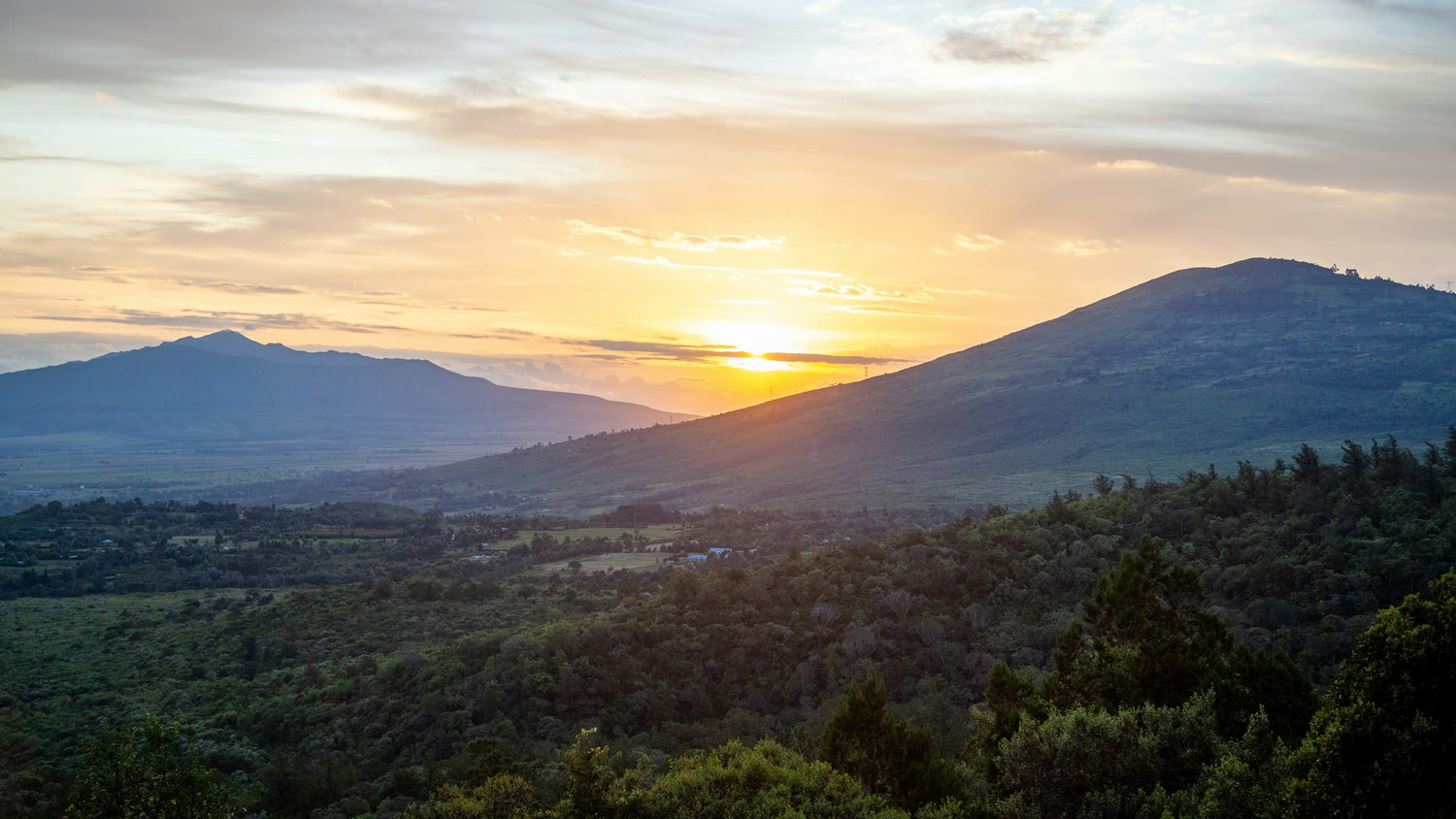 Sunset over a mountainous landscape with trees and clouds.